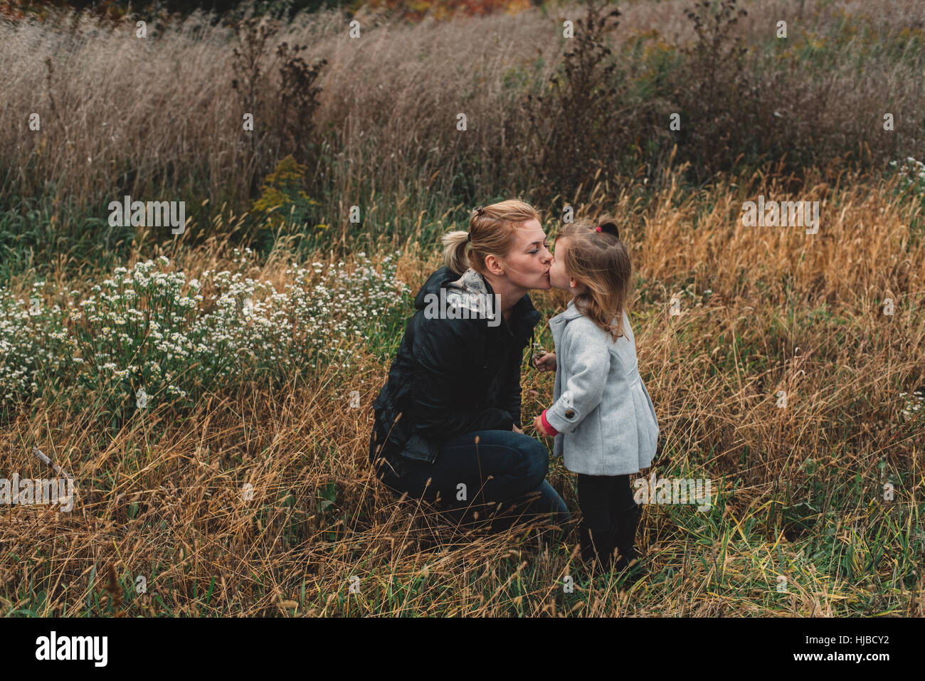 Mitte Erwachsene Frau küssen Kleinkind Tochter im Feld lange Gras Stockfoto
