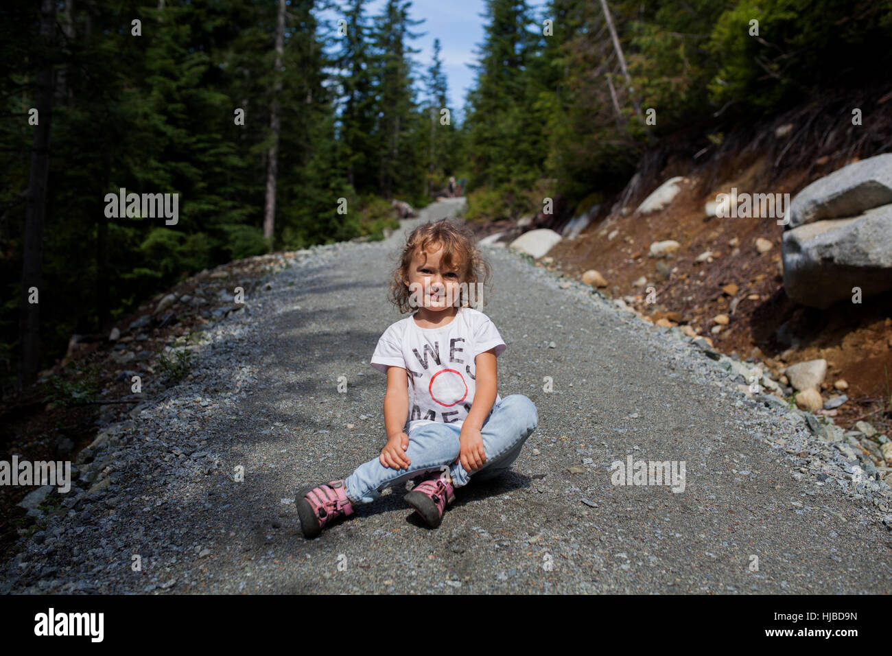 Kleines Mädchen sitzt auf Schotterstraße im Wald, Vancouver, Britisch-Kolumbien, Kanada Stockfoto