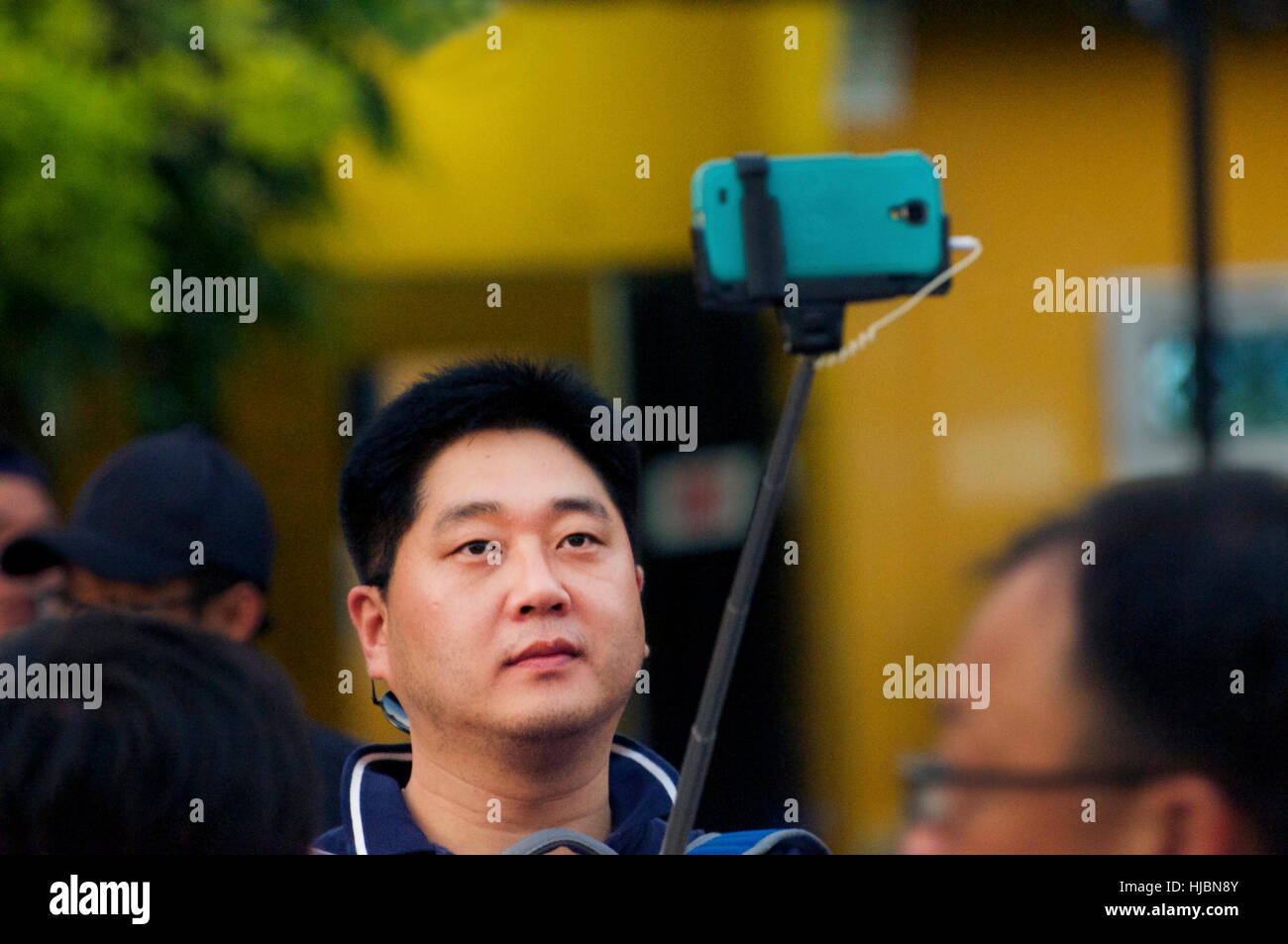 Asien-Tourist nimmt Selfie mit grünen iPhone auf Stick vor gelben Gebäude in der Altstadt von Hoi an, Vietnam. Ein UNESCO-Weltkulturerbe Stockfoto