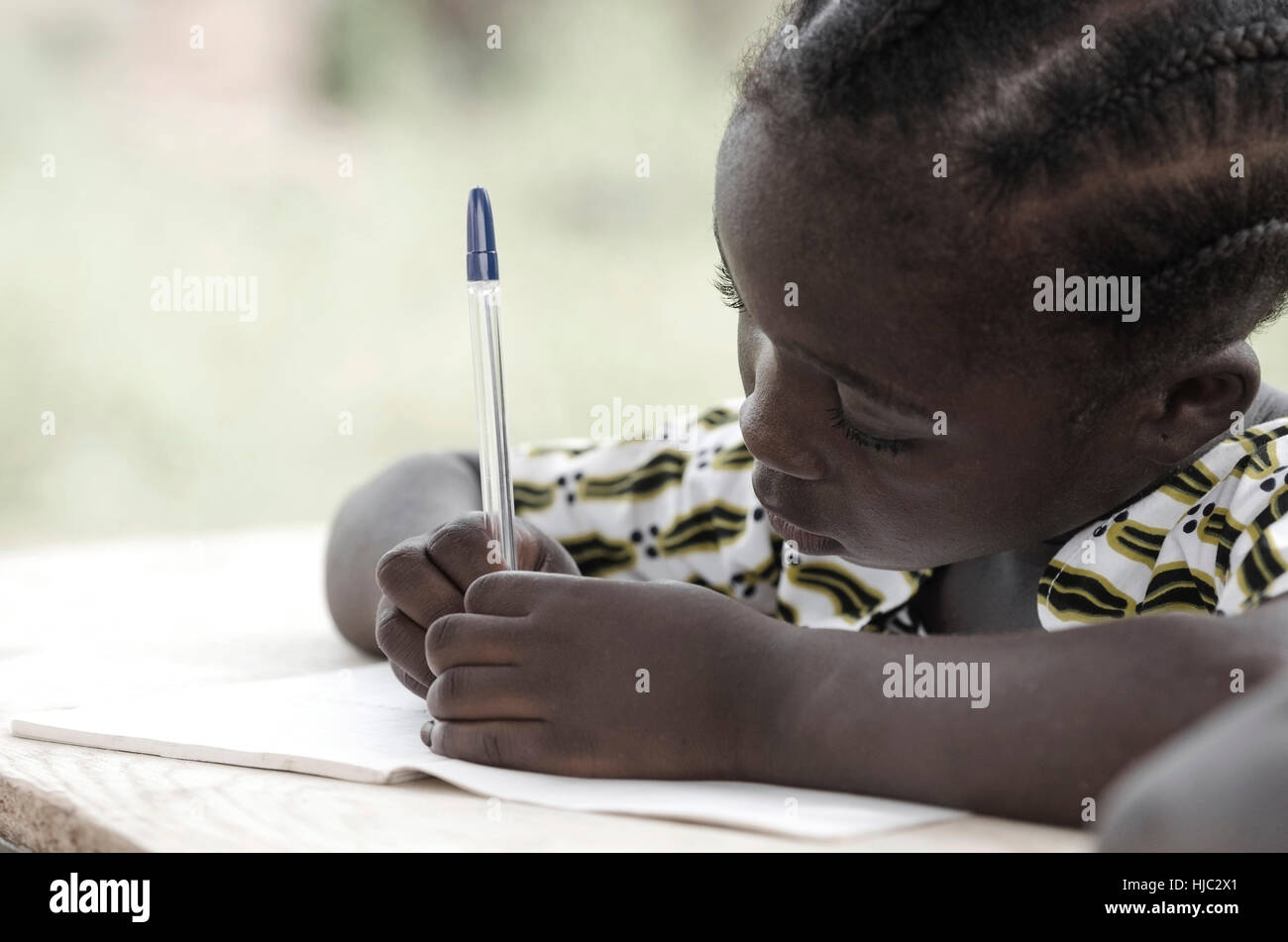 Niedlichen afrikanischen Schülerin ihre Hausaufgaben in der Schule: schöne schwarze Mädchen schreiben und lernen mit einem blauen Stift. Sie sitzt in ihrem Schreibtisch zu tun Stockfoto