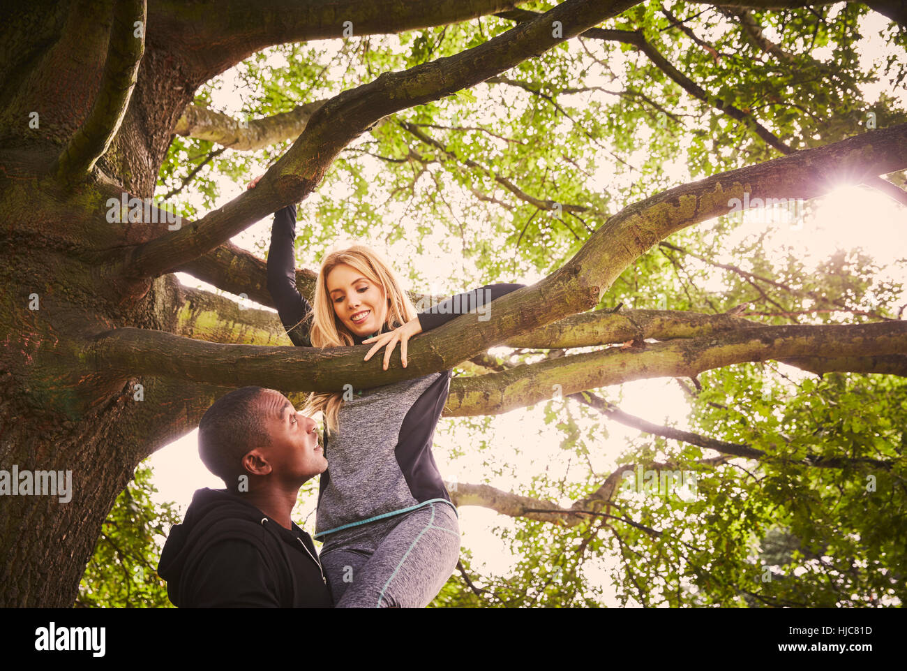 Personaltrainer heben junge Frau um Parkbaum Klettern Stockfoto
