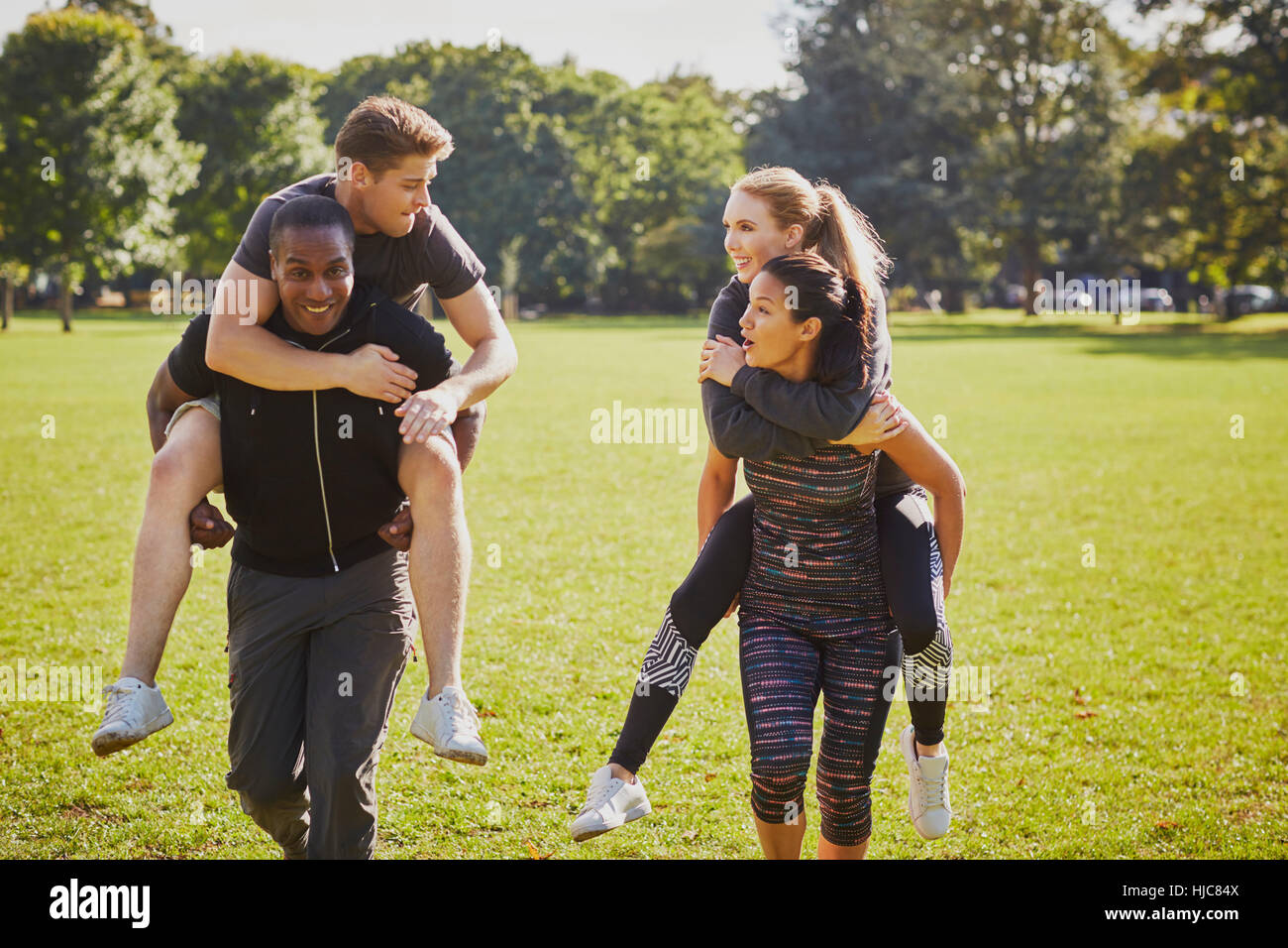 Männer und Frauen, die Spaß im Park, mit Huckepack-Rennen training Stockfoto
