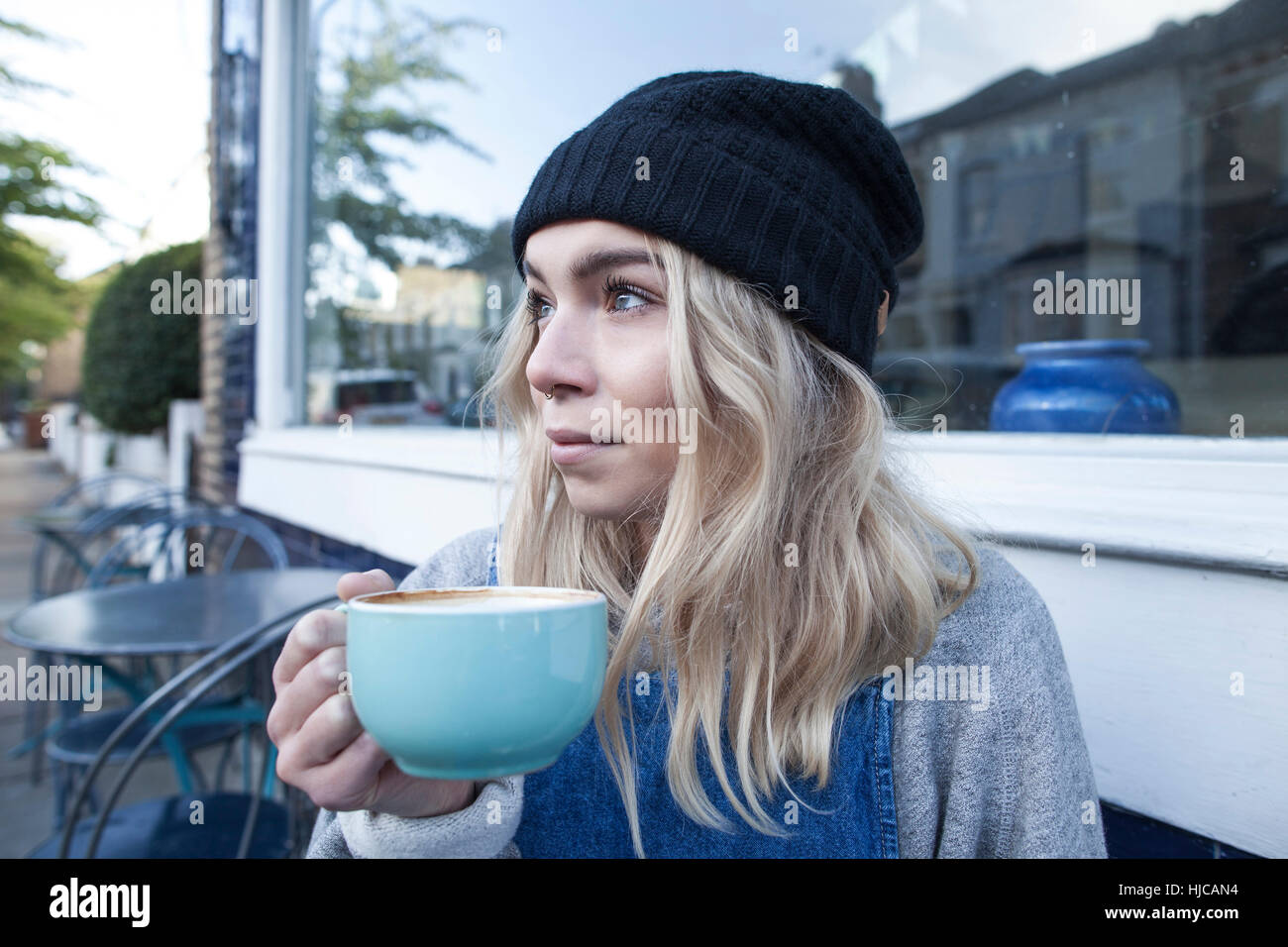 Junge Frau sitzt vor Café, Tasse Tee trinken Stockfoto