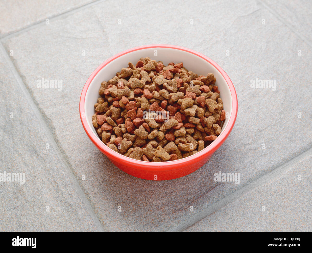 Roten Tiernahrung Schale voll trocken Katzenfutter auf einem grauen Fliesenboden Stockfoto