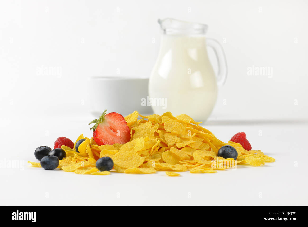 Krug mit Milch und Cornflakes mit Beeren auf weißem Hintergrund Stockfoto