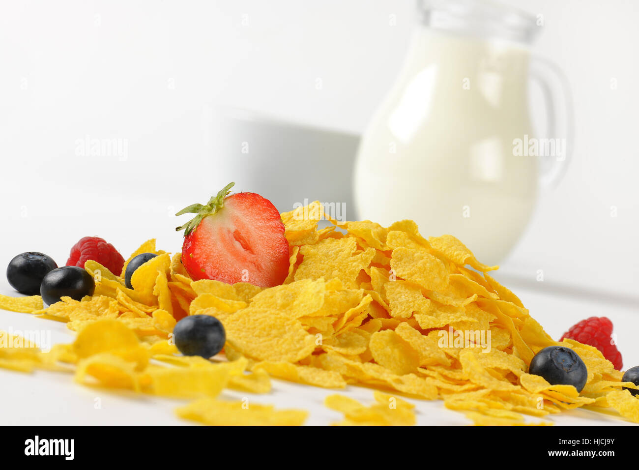 Krug Milch und Cornflakes mit Beeren auf weißem Hintergrund - Nahaufnahme Stockfoto