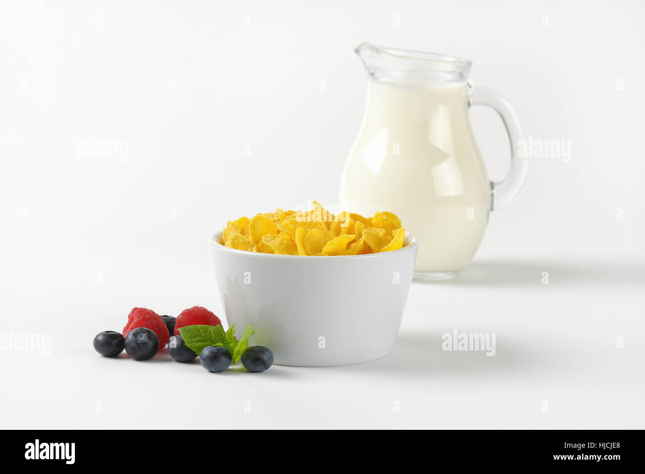 Schüssel mit Cornflakes und Krug Milch auf Wollweiß Hintergrund mit Schatten Stockfoto
