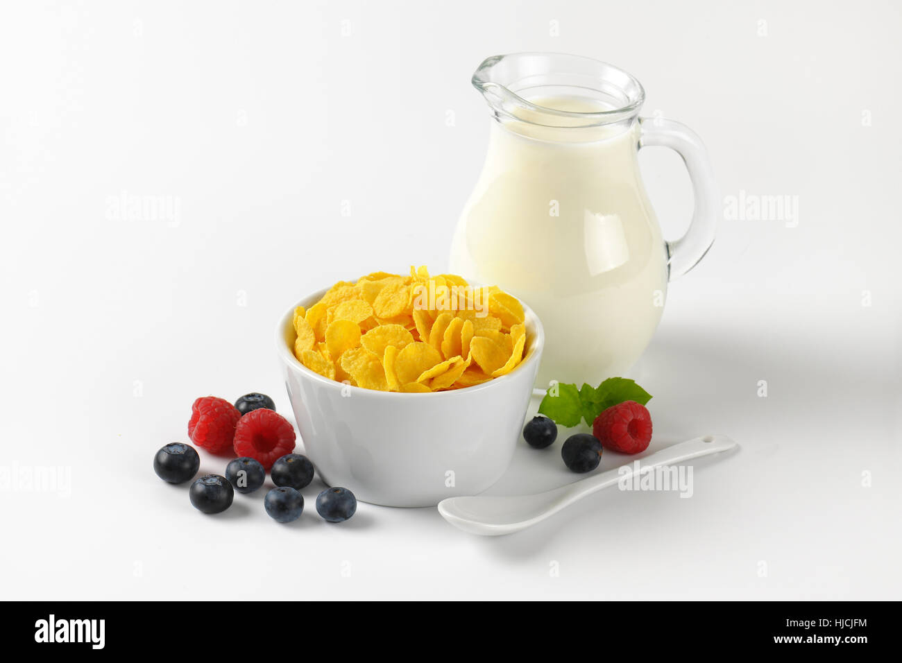 Schüssel mit Cornflakes und Krug Milch auf weißem Hintergrund Stockfoto