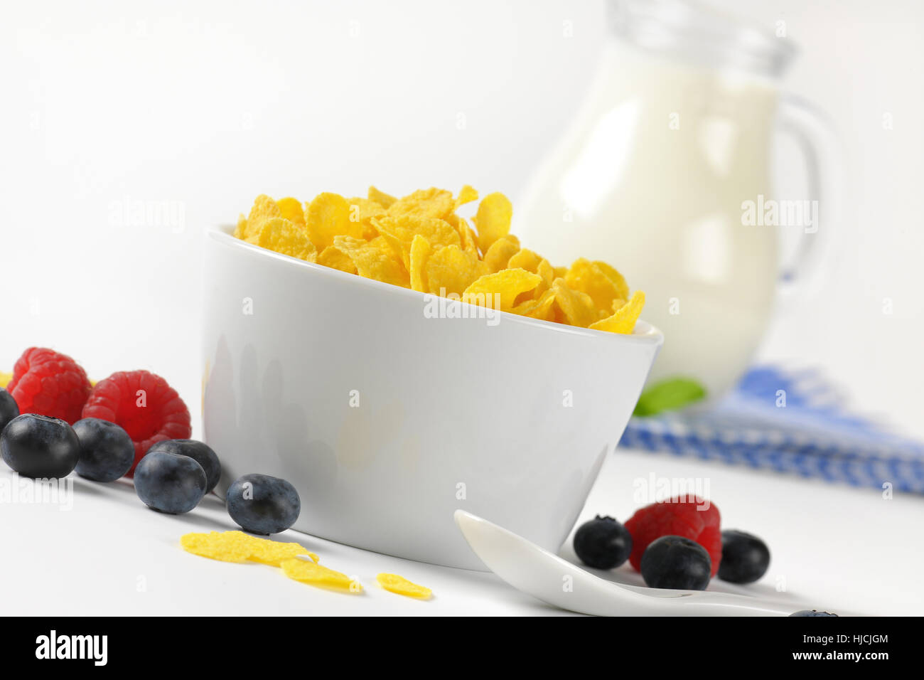 Schüssel mit Cornflakes und Krug Milch auf kariertem Geschirrtuch - Nahaufnahme Stockfoto