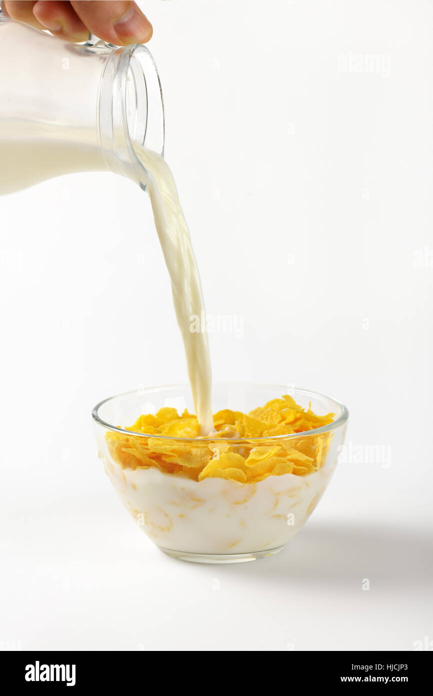 Milch Eingießen in Schüssel Cornflakes auf weißem Hintergrund Stockfoto