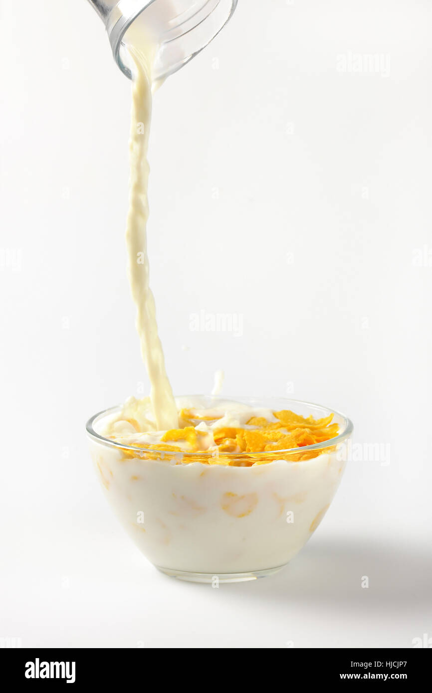 Milch Eingießen in Schüssel Cornflakes auf auf Wollweiß Hintergrund mit Schatten Stockfoto