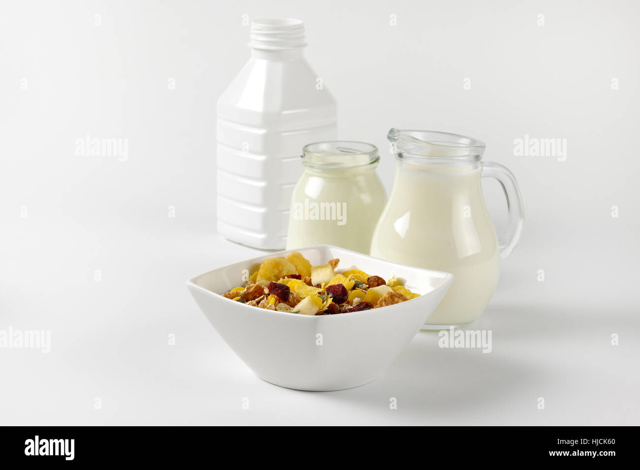 Schüssel mit Haferflocken mit Milch und Joghurt auf Wollweiß Hintergrund mit Schatten Glas Krug Stockfoto