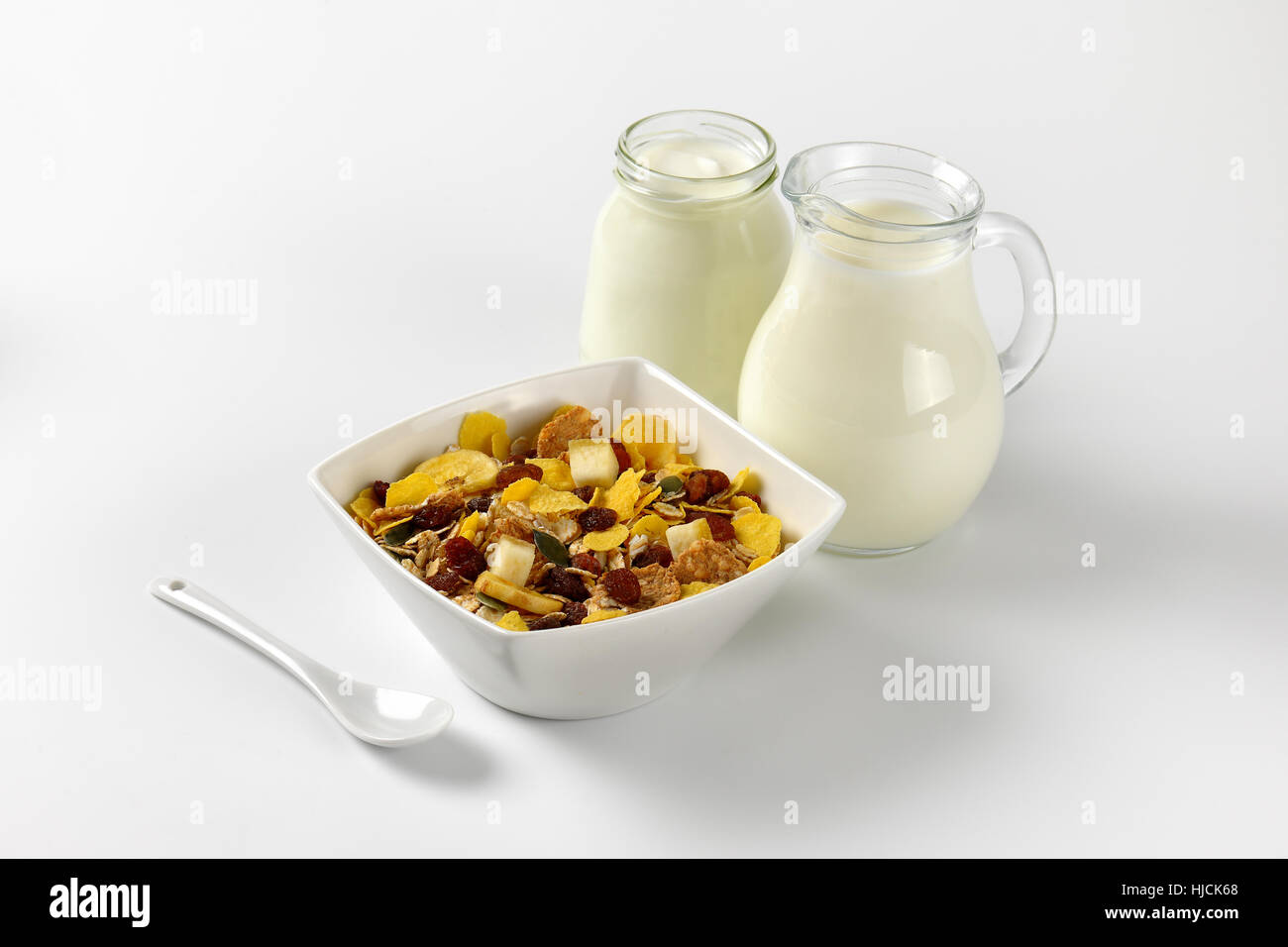 Schüssel mit Haferflocken mit Milch und Joghurt auf Wollweiß Hintergrund mit Schatten Glas Krug Stockfoto