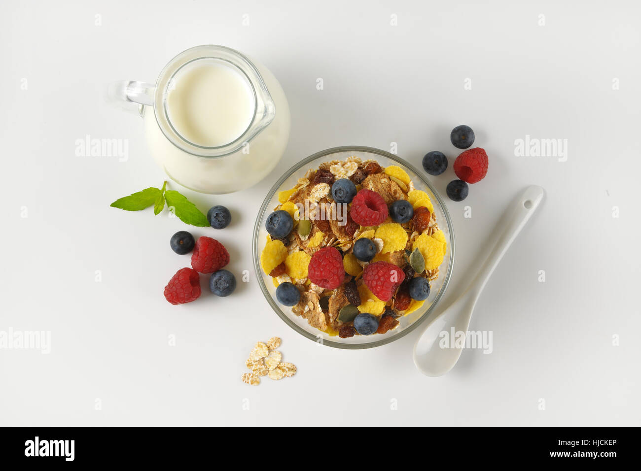 Schüssel mit Getreide und Beerenfrucht mit Milchkanne Milch auf Wollweiß Hintergrund mit Schatten Stockfoto