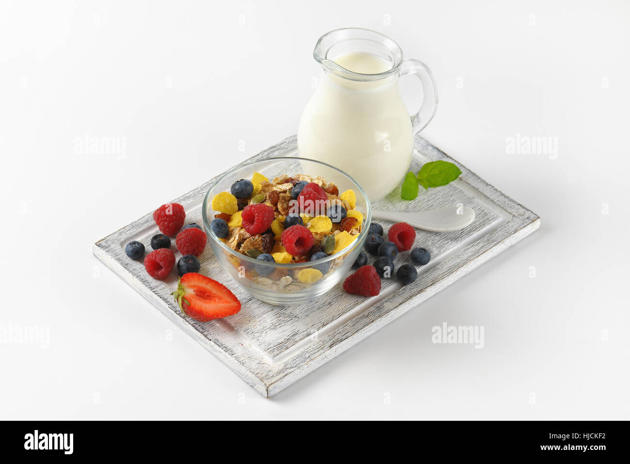 Schüssel mit Getreide und Beerenfrucht mit Milchkanne Milch auf Holzbrett Stockfoto