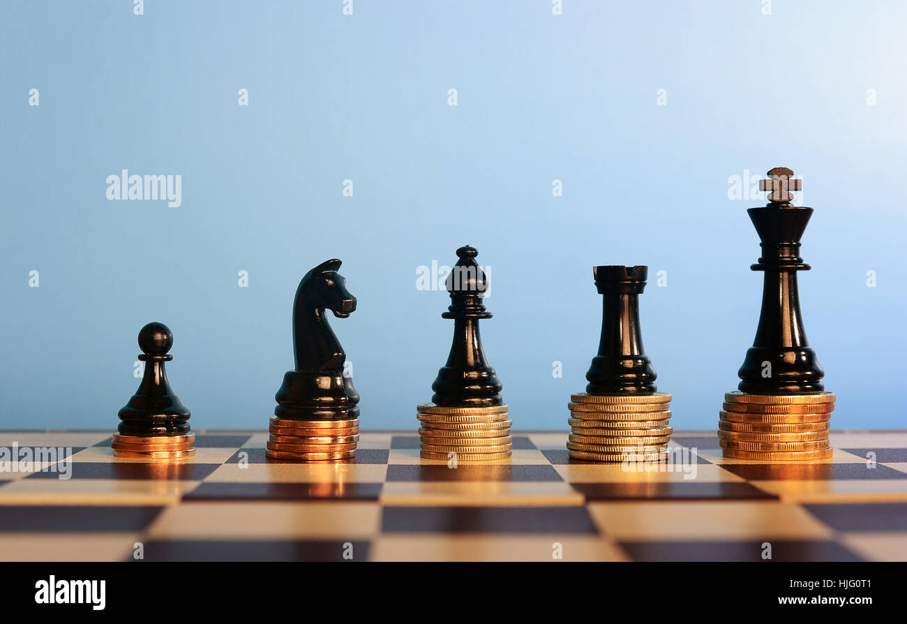 Schachfiguren auf gestapelten Münzen vor blauem Hintergrund, Business-Konzept Stockfoto