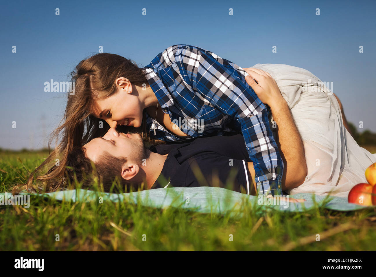 Mädchen liegen oben auf den Kerl und küsst ihn. Paar mit einem Picknick auf einem grünen Rasen Stockfoto