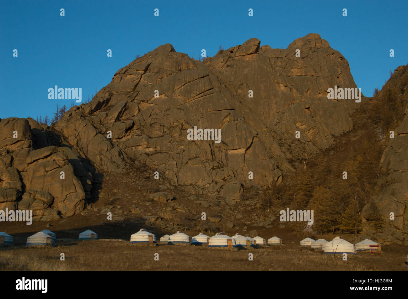 Ein Lager mit mehreren weißen Jurten an der Basis des robusten Stein Berge, die einen satten Braun in den Sonnenuntergang. Das Hotel liegt in der Mongolei. Stockfoto