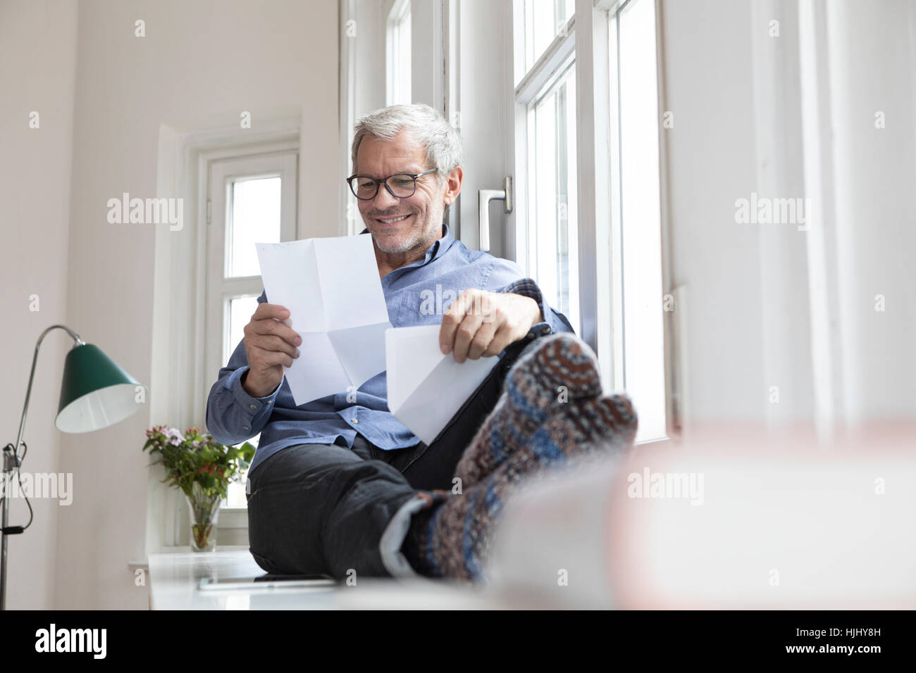 Reifer Mann zu Hause sitzen am Fenster lesen von Dokumenten Stockfoto