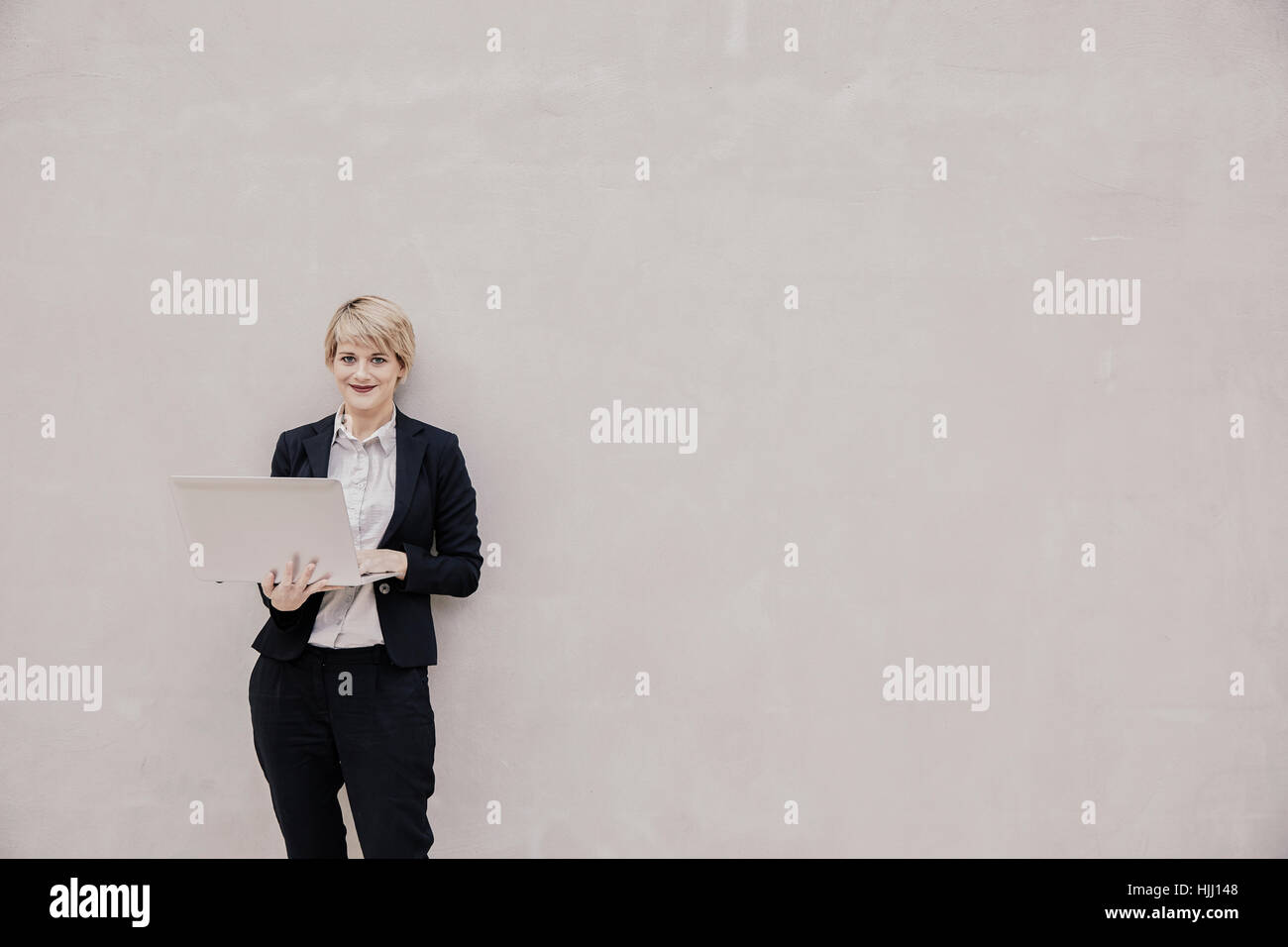 Lächelnd Geschäftsfrau mit Laptop stand vor Betonwand Stockfoto