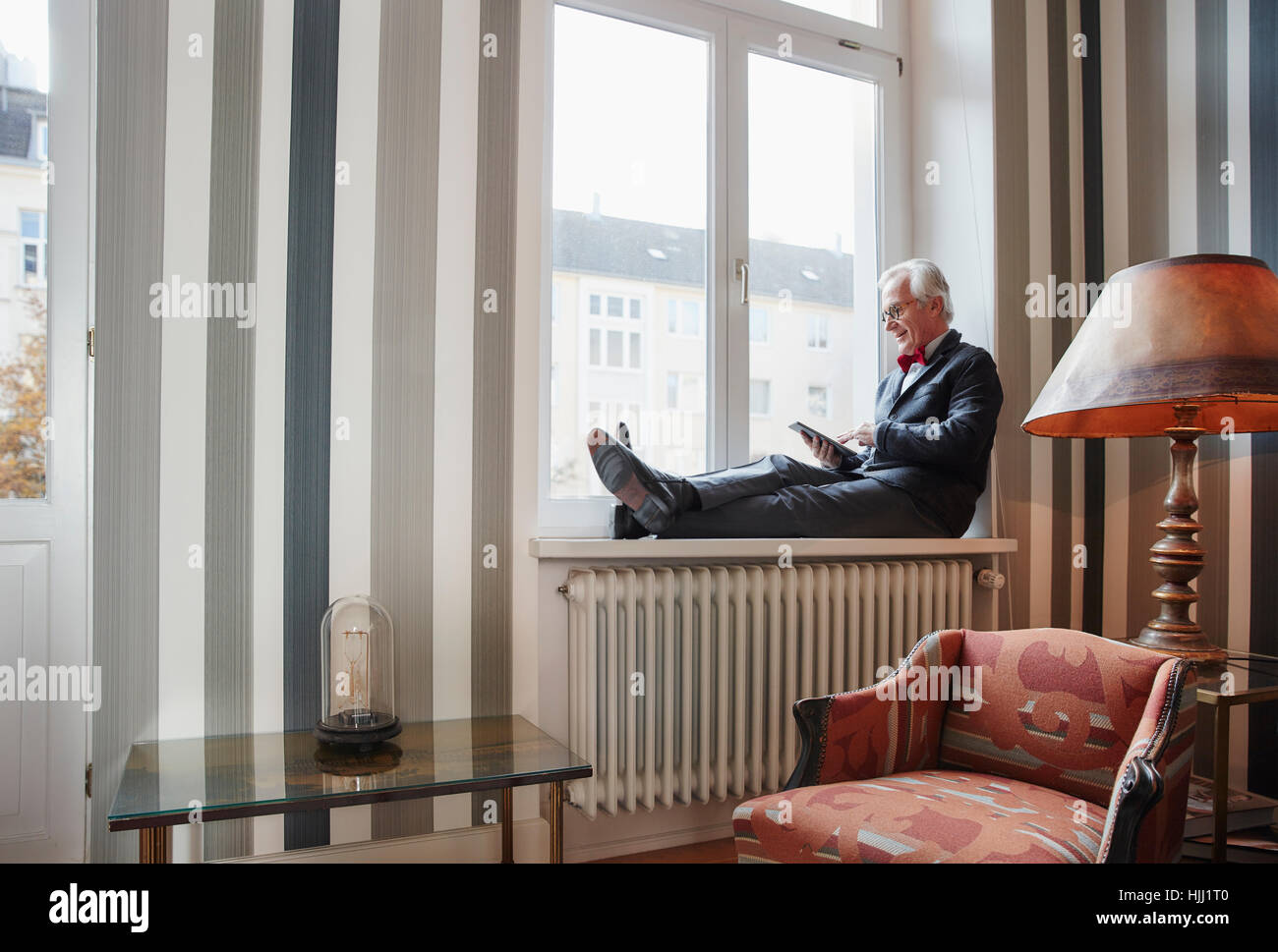 Ältere Mann sitzt in der Fensterbank mit tablet Stockfoto
