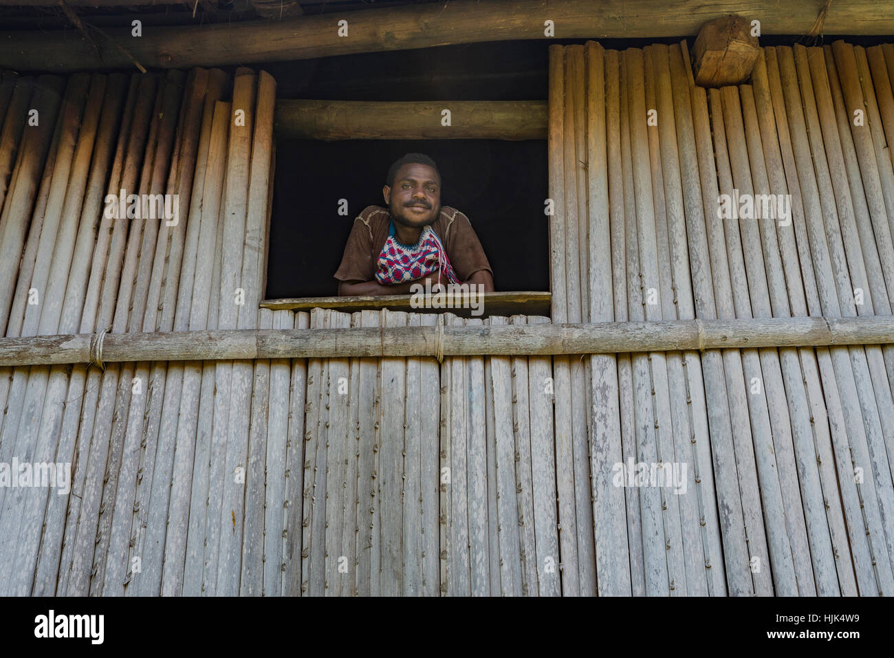 Porträt eines Mannes, der Blick aus dem Fenster eines Holzhauses, hergestellt aus Bambus in einem Dorf auf dem Sepik River, Papua New Guinea Stockfoto