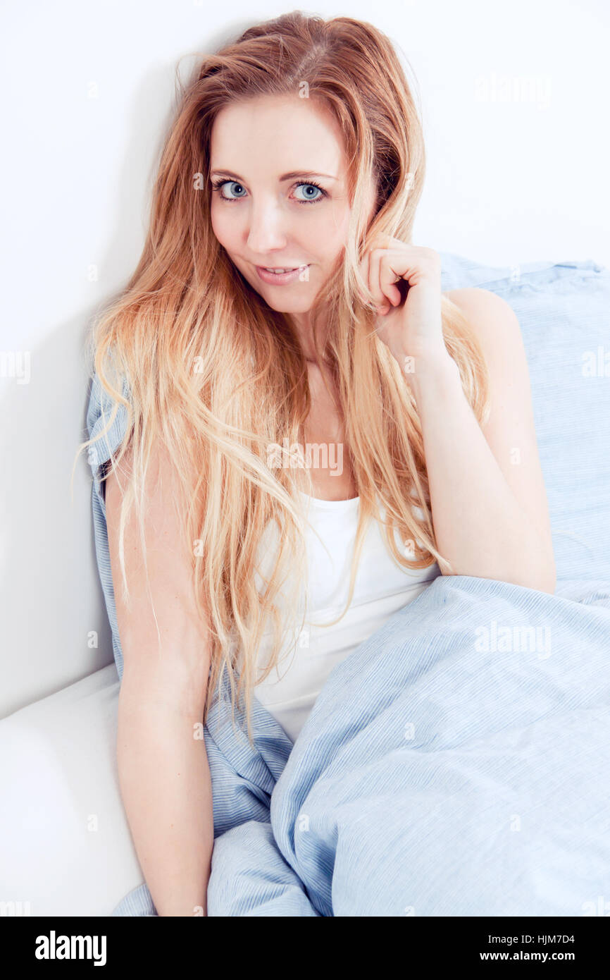 junge blonde hübsche Frau im Bett mit Kissen Stockfoto
