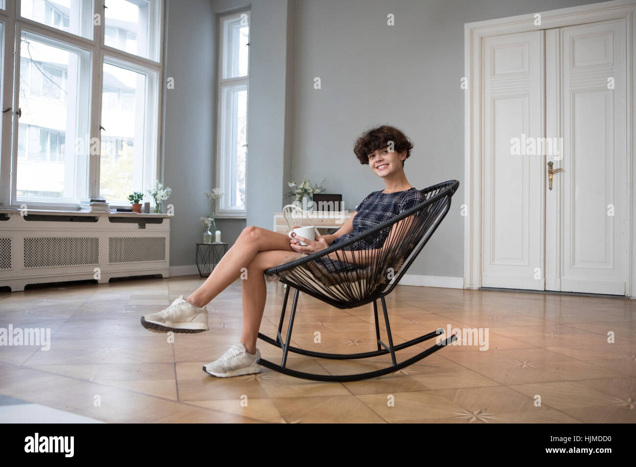 Porträt der lächelnde junge Frau sitzt im Schaukelstuhl zu Hause Stockfoto