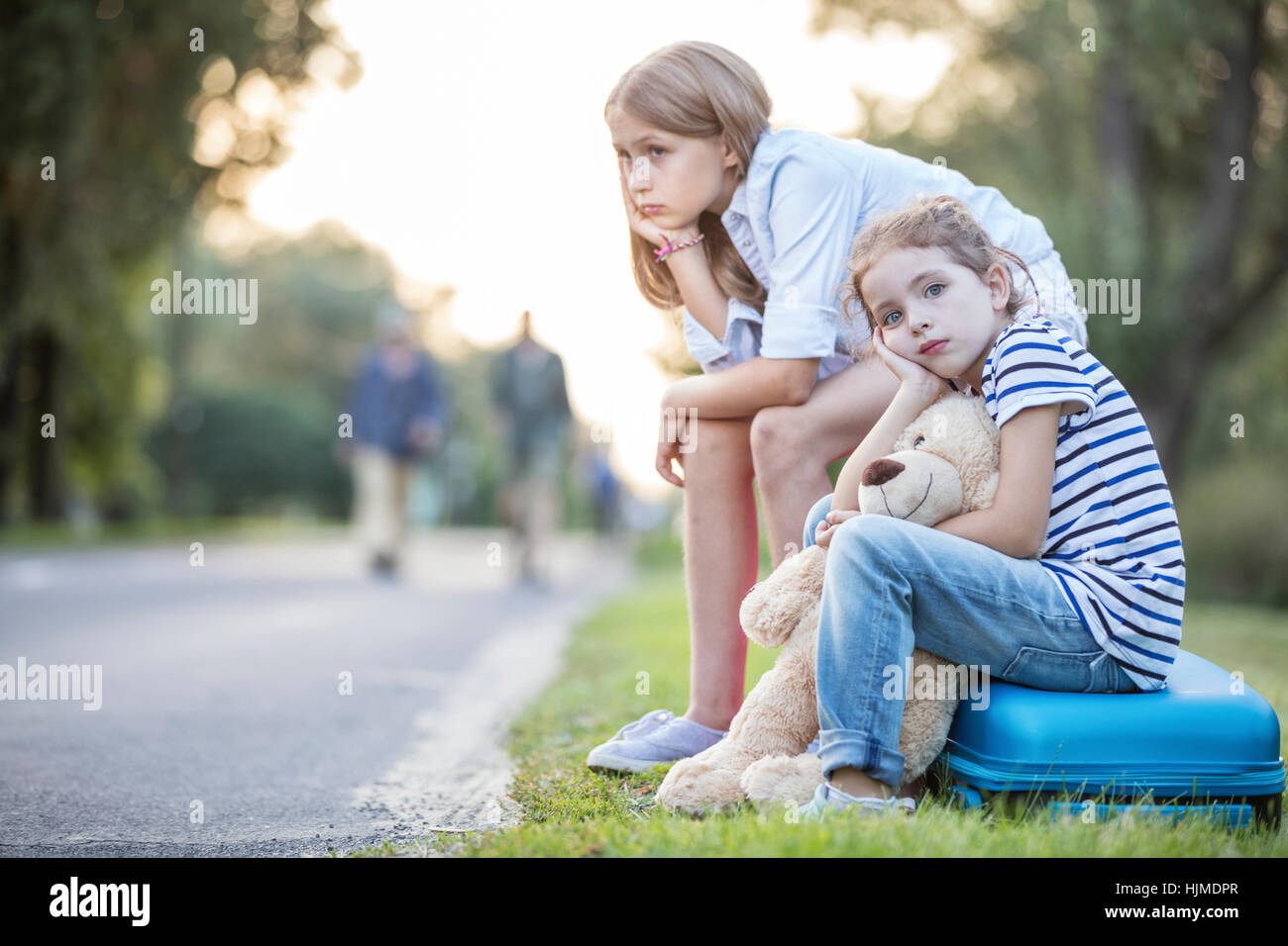 Zwei Mädchen sitzen auf Koffer am Straßenrand Stockfoto