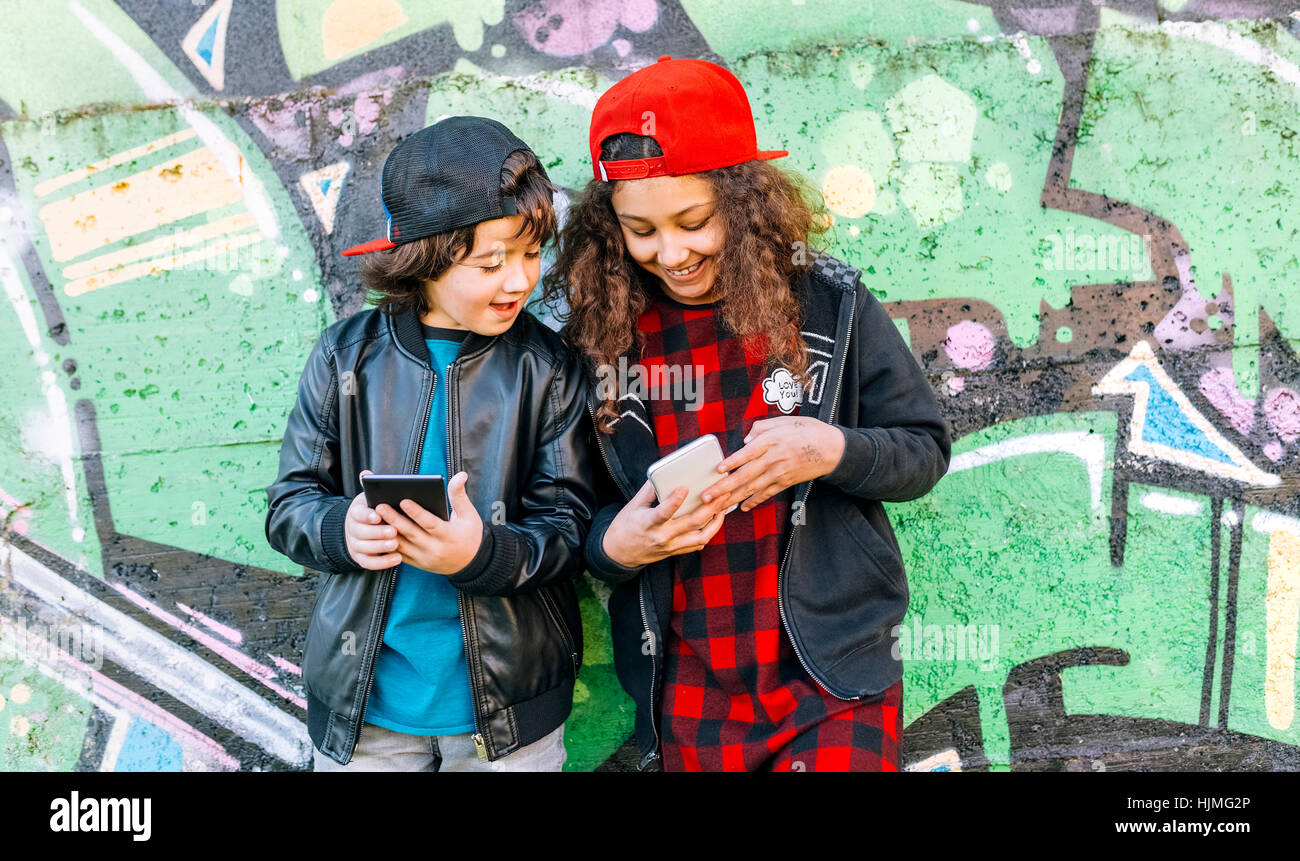 Zwei Kinder stehen vor Graffitiwand Blick auf Handy Stockfoto