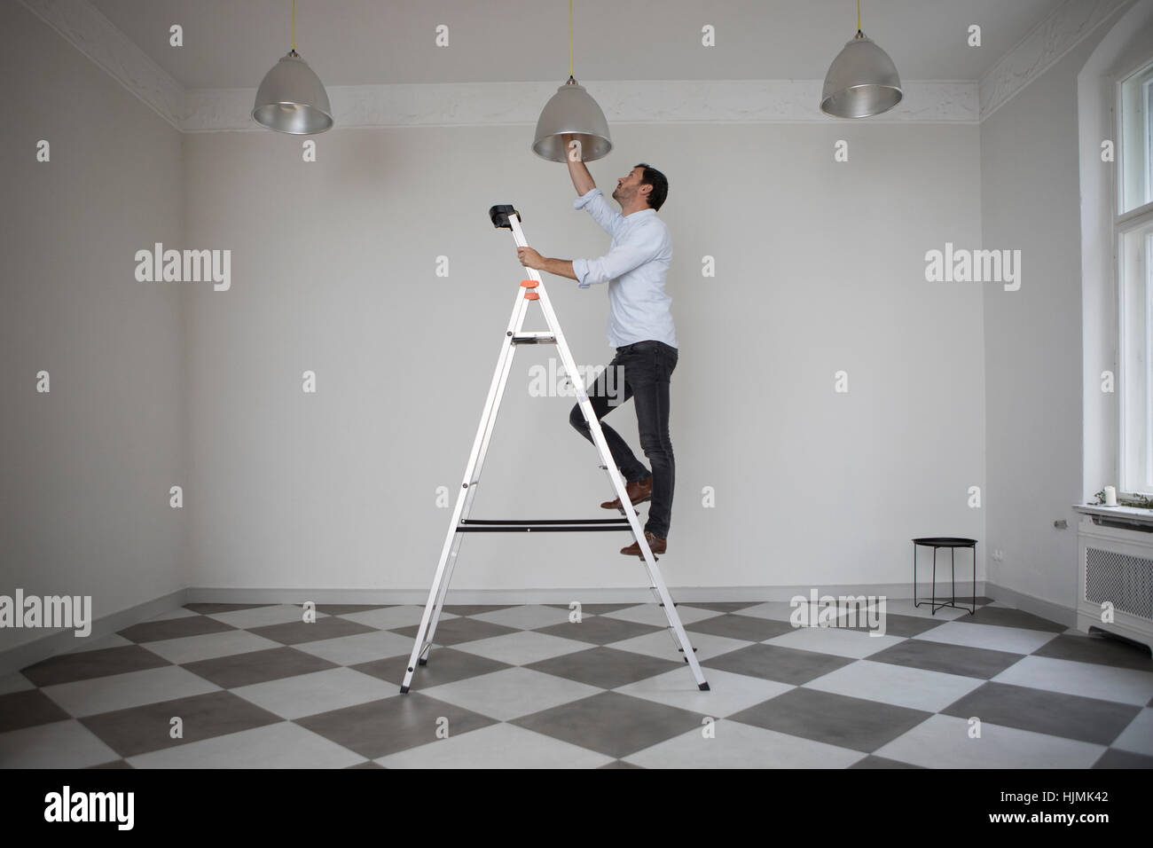 Mann steht auf Leiter in einem leeren Raum ändern Lampe Deckenleuchte Stockfoto