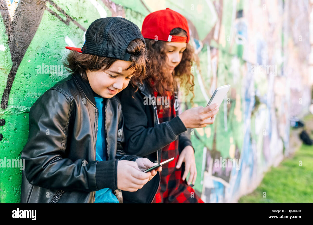 Zwei Kinder mit Smartphones Graffitiwand gelehnt Stockfoto