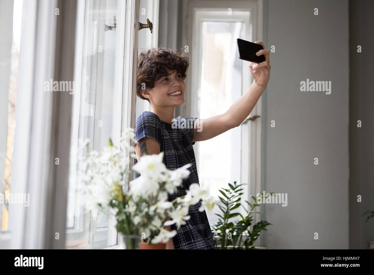Lächelnde junge Frau stand vor-Fenster unter Selfie mit smartphone Stockfoto