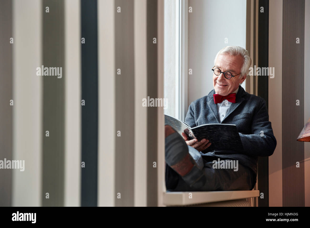 Ältere Mann sitzt in der Fensterbank Lesung Magazin Stockfoto