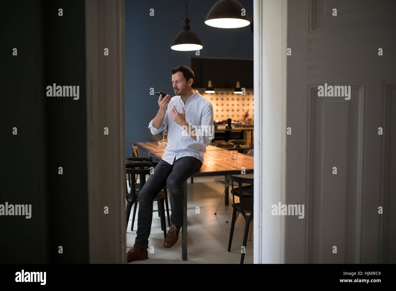 Mann am Telefon sitzen am Tisch in seiner Küche Stockfoto
