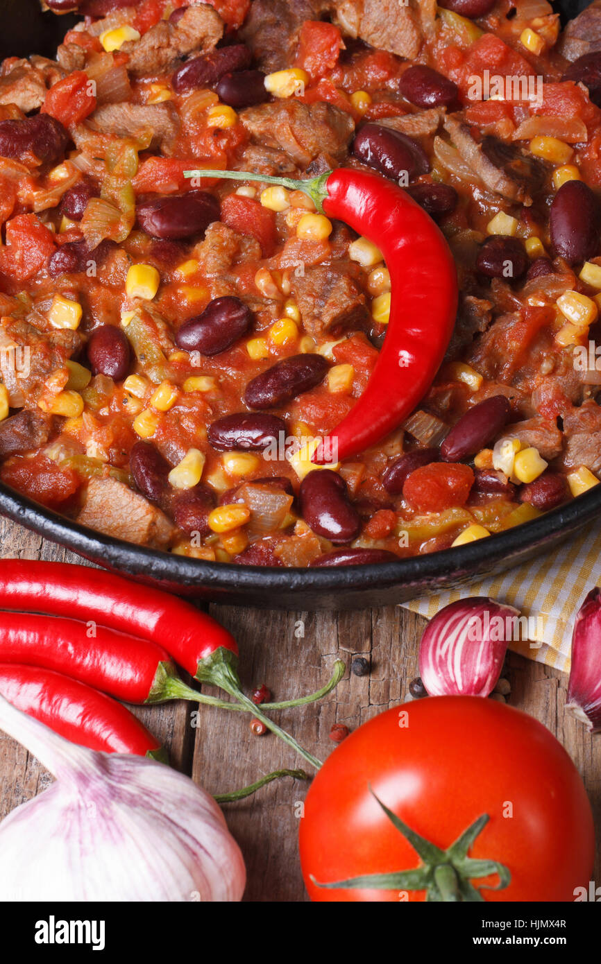 Mexikanisches Chili Con Carne Nahaufnahme in einer Pfanne auf einem hölzernen Hintergrund mit den Zutaten. vertikale Ansicht von oben Stockfoto