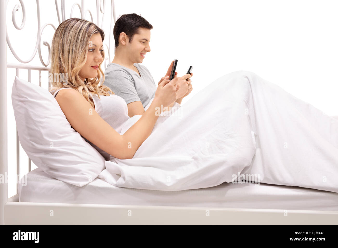 Junges Paar im Bett liegend und mit Blick auf ihren Mobiltelefonen isoliert auf weißem Hintergrund Stockfoto