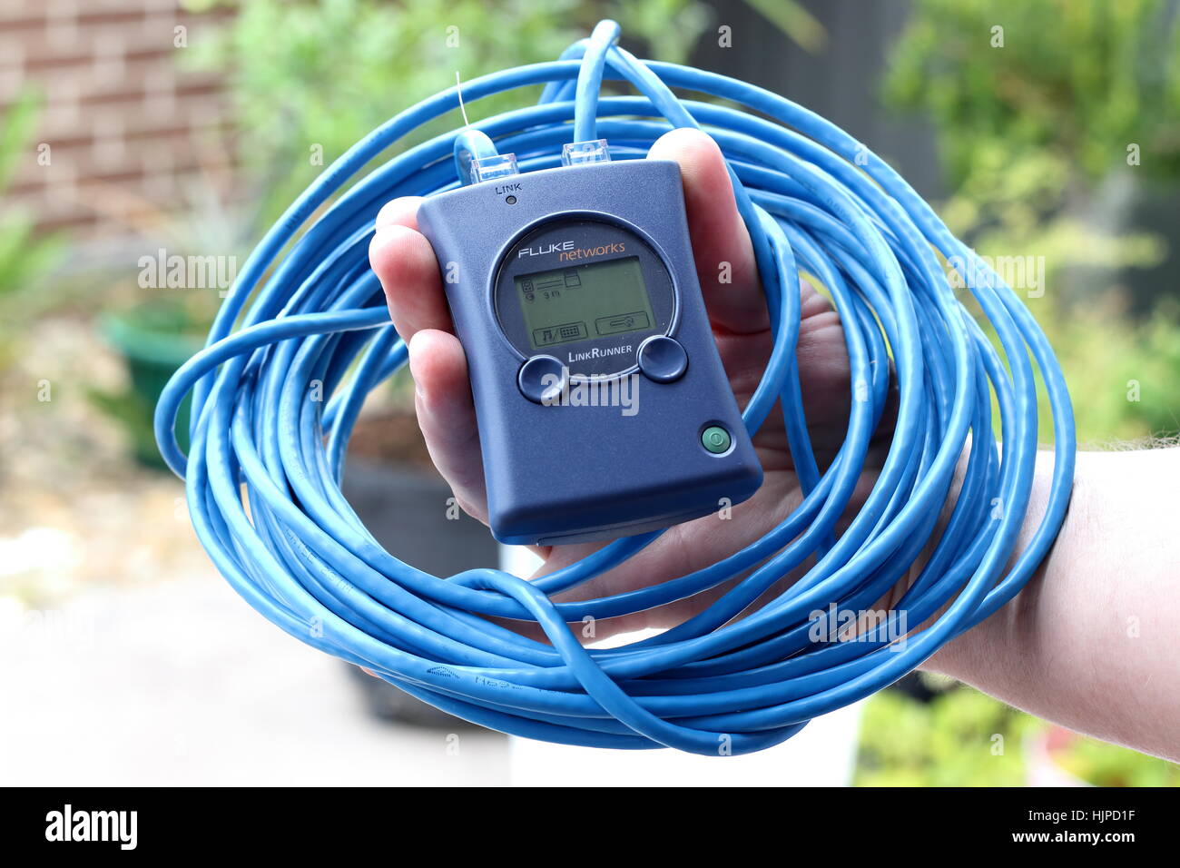 Hand mit Fluke Networks LinkRunner Gerät mit blauen Kabeln Stockfoto