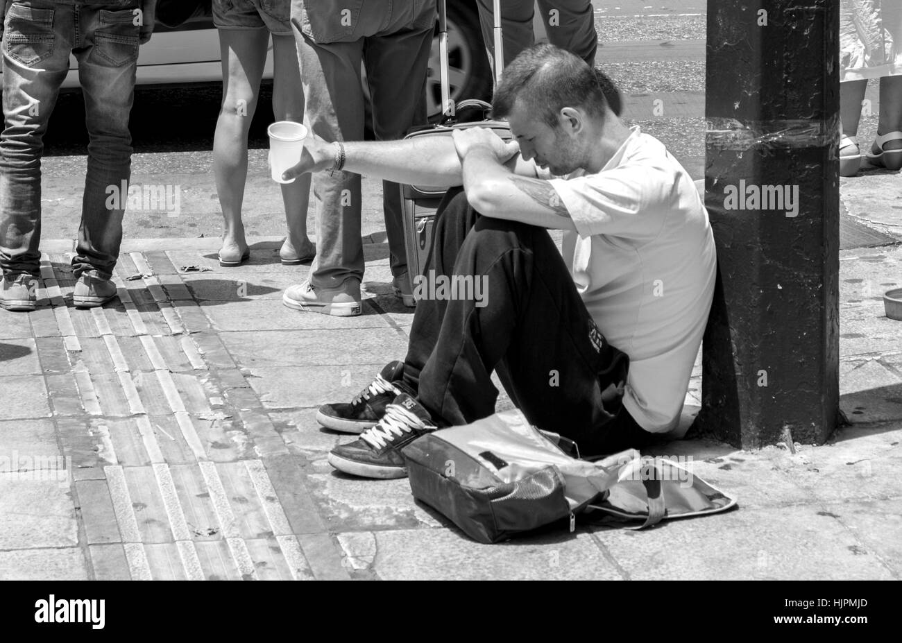 Eine junge männliche sitzen seine Tasse halten, wie er für Geld in Athen, Griechenland bettelt. Stockfoto