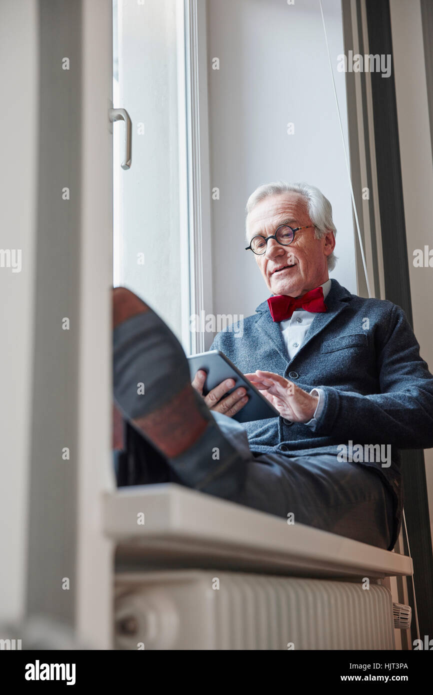 Ältere Mann sitzt in der Fensterbank mit tablet Stockfoto