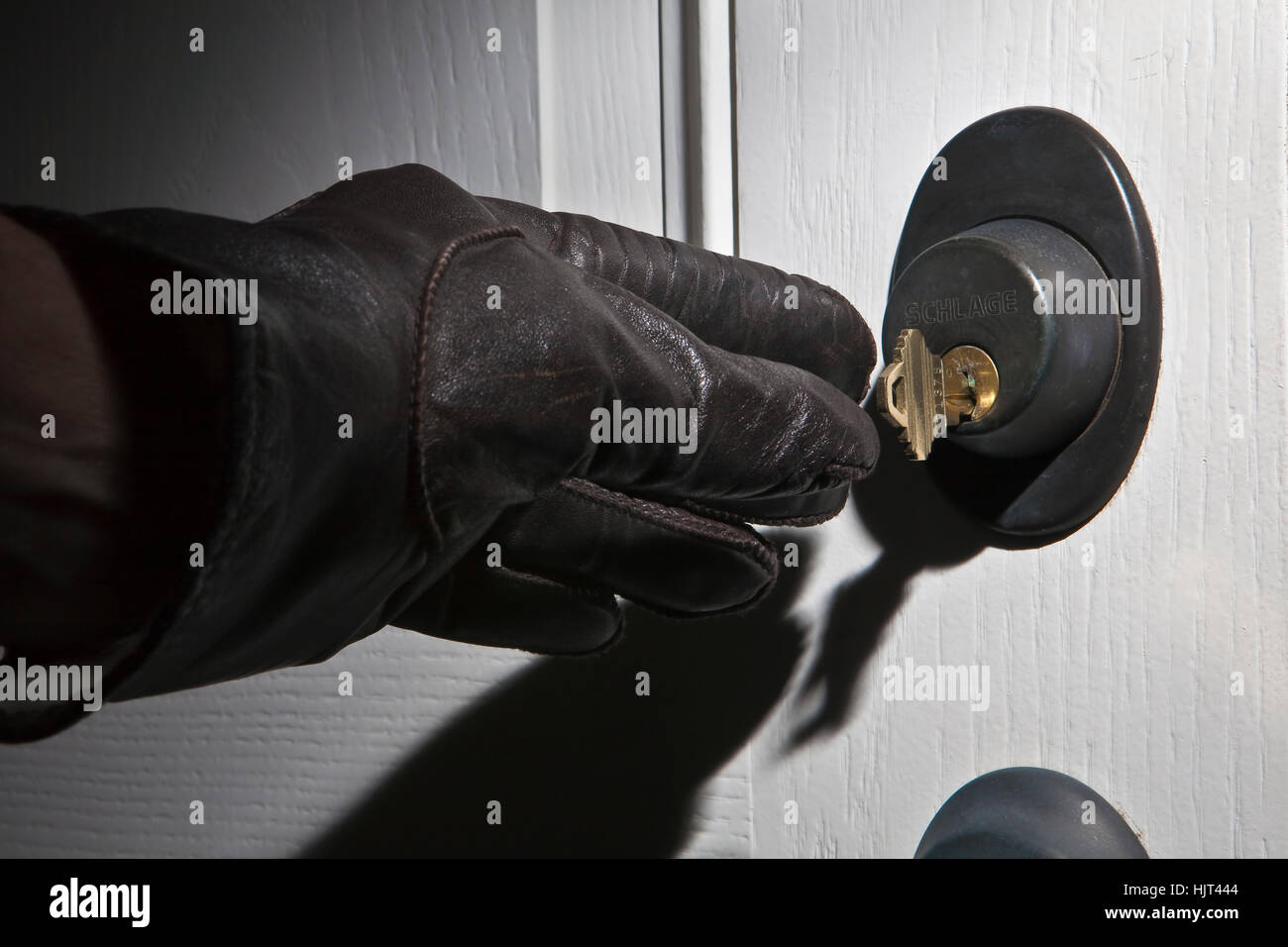 Leder-behandschuhten Hand greift für Hausschlüssel im Schloss der weißen Tür Stockfoto