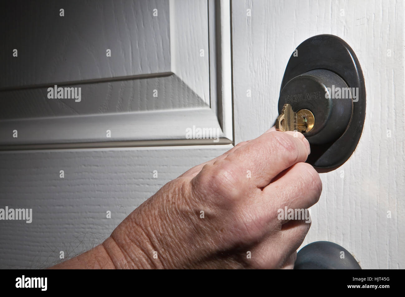 Älterer Mann Hand drehen Hausschlüssel im Schloss der weißen Tür Stockfoto