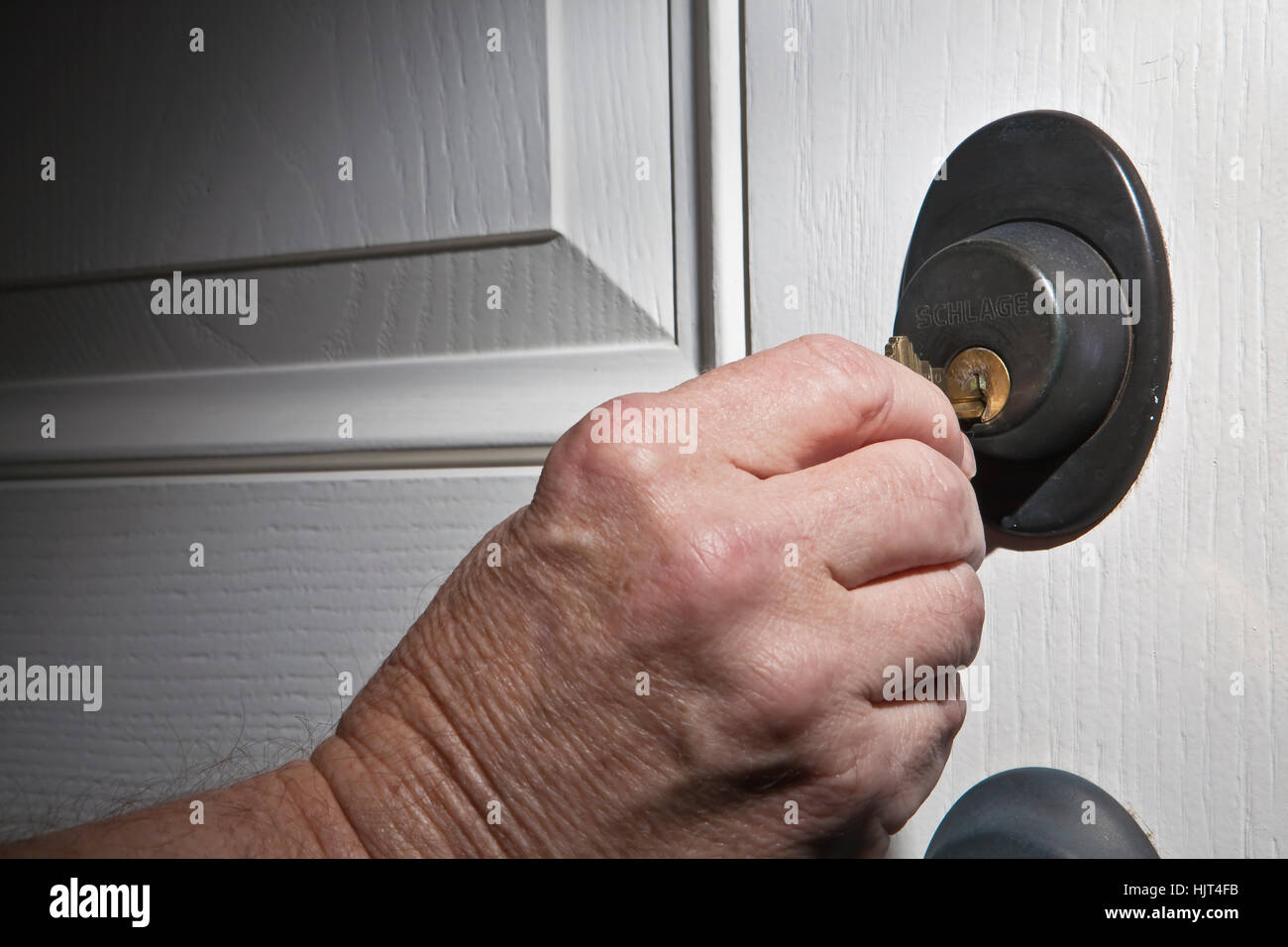 Älterer Mann Hand nehmen Haus von Schlüssel oder Hausschlüssel in, indem der weiße Tür verriegeln Stockfoto