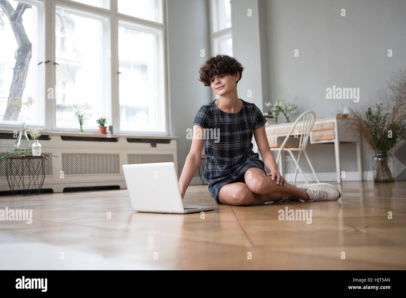 Junge Frau sitzt auf dem Boden zu Hause mit Blick auf laptop Stockfoto