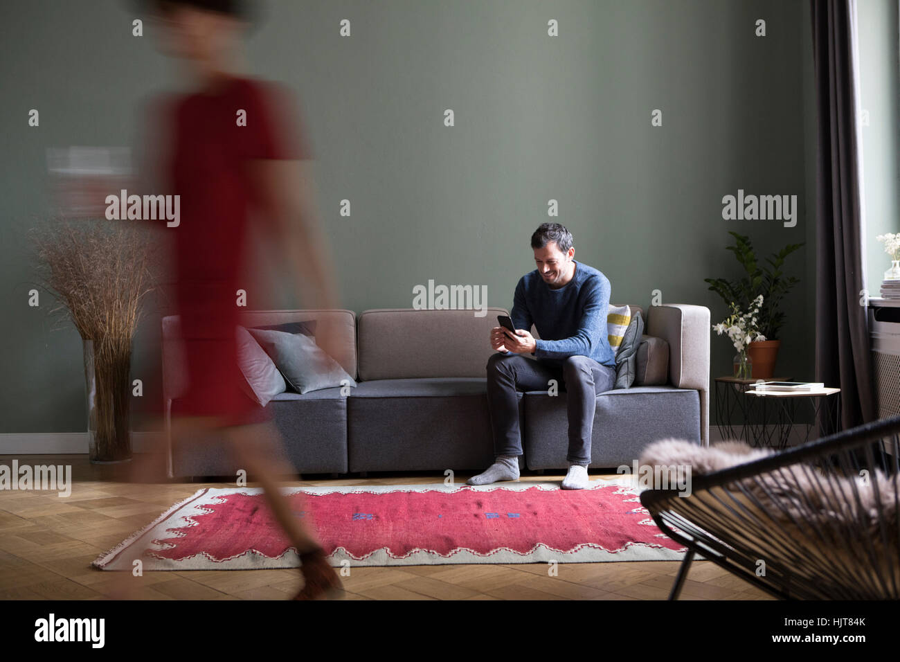 Mann sitzt auf der Couch im Wohnzimmer, während seine Freundin vorbei in den Vordergrund Stockfoto