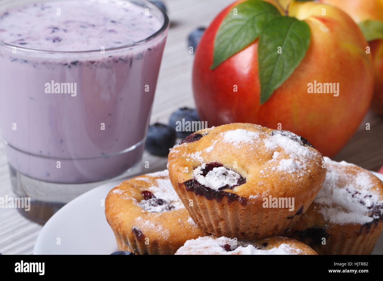 Blaubeer-Muffins, frische Pfirsiche und ein Milchshake Closeup auf einem Holztisch. horizontale Stockfoto