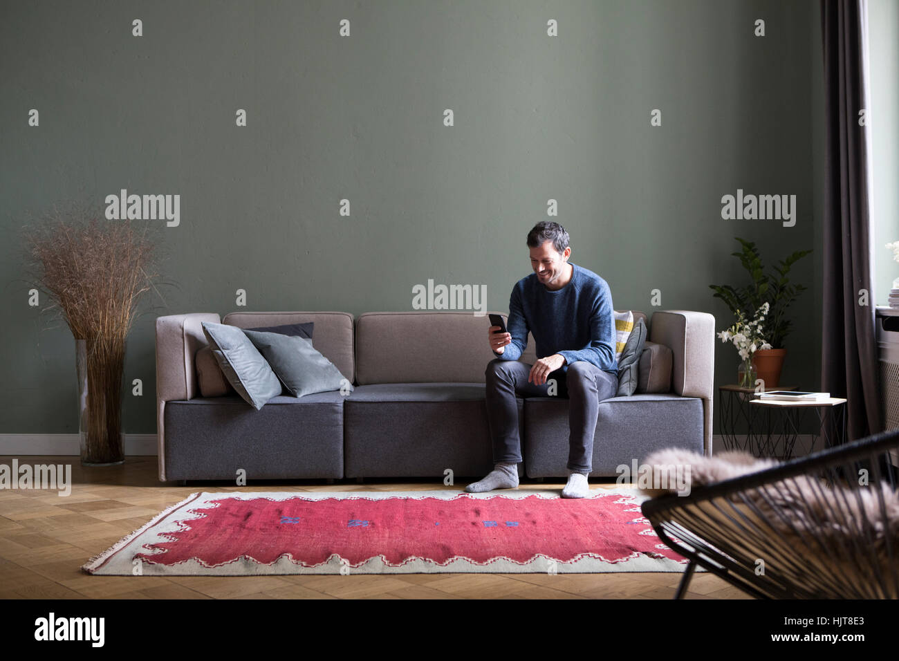 Mann sitzt auf der Couch in seinem Wohnzimmer Blick auf smartphone Stockfoto