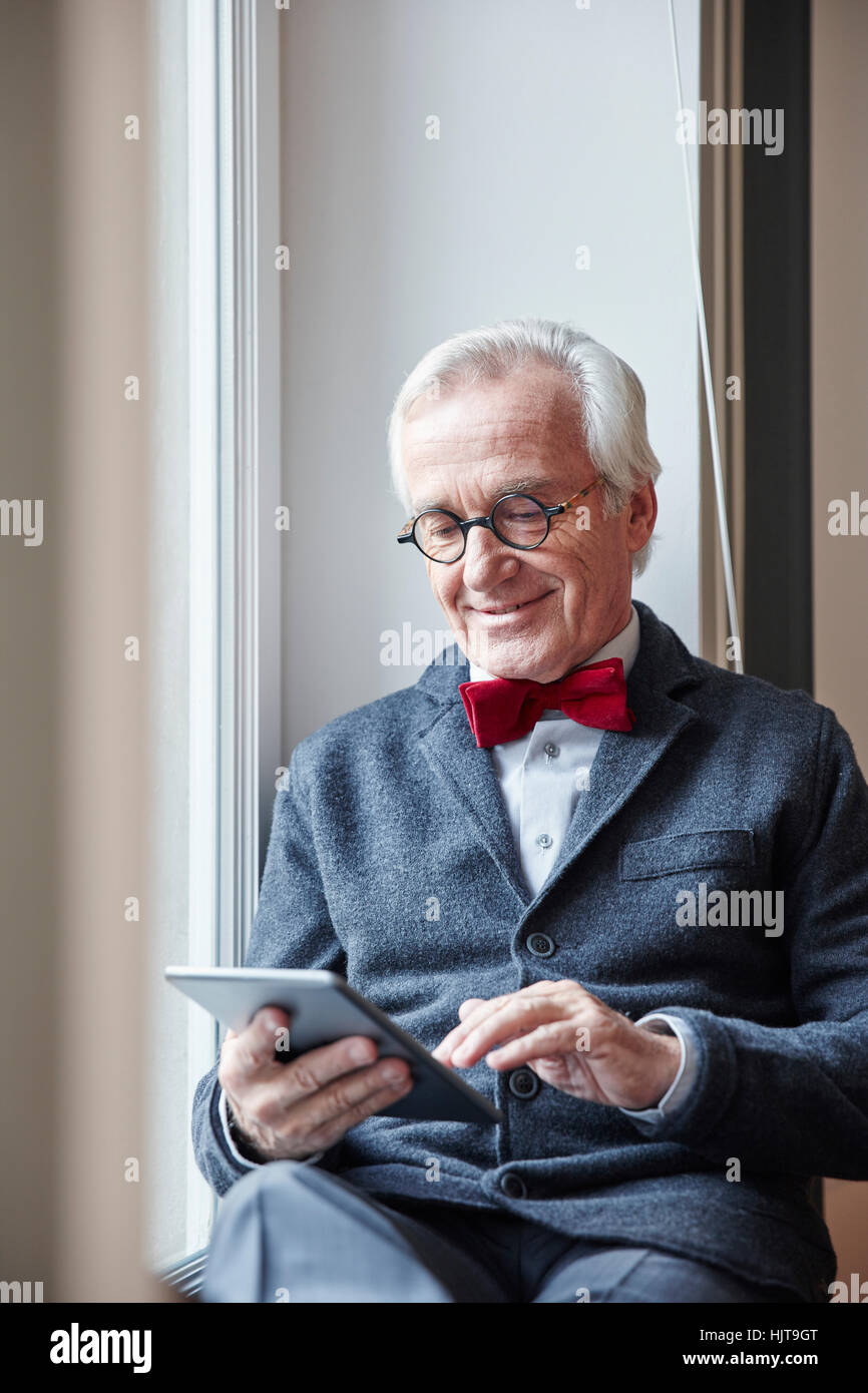 Lächelnde senior Mann sitzt in der Fensterbank mit tablet Stockfoto