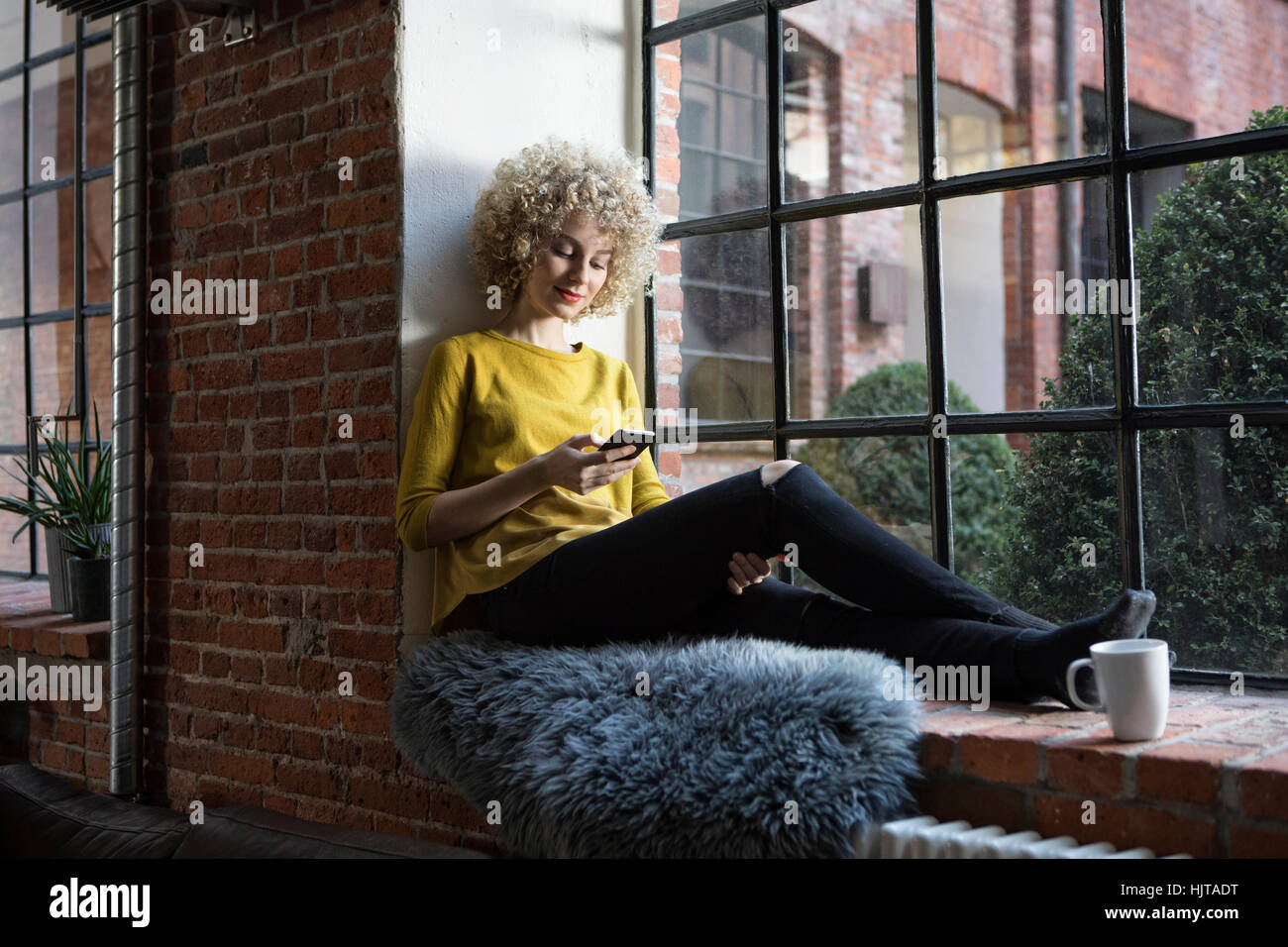 Junge Frau sitzt auf der Fensterbank, mit Smartphone Stockfoto