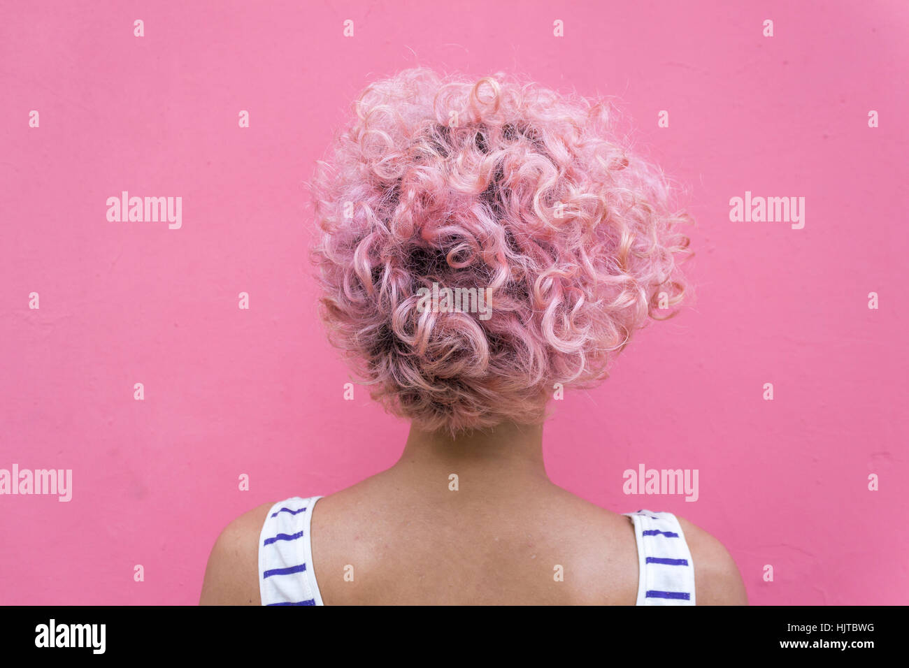 Junge Frau mit kurzen rosa locken stehen gegen Rosa Wand mit zurückgedreht Stockfoto